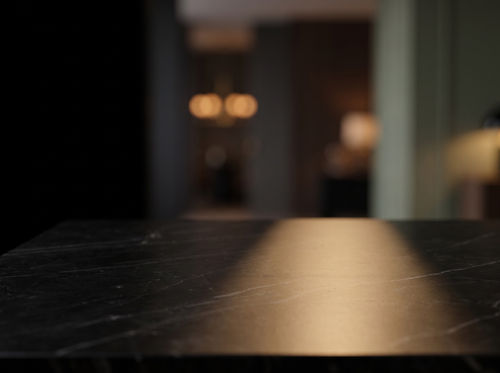 A dark polished marble surface lit from one side, with a warm, out-of-focus interior behind it.
